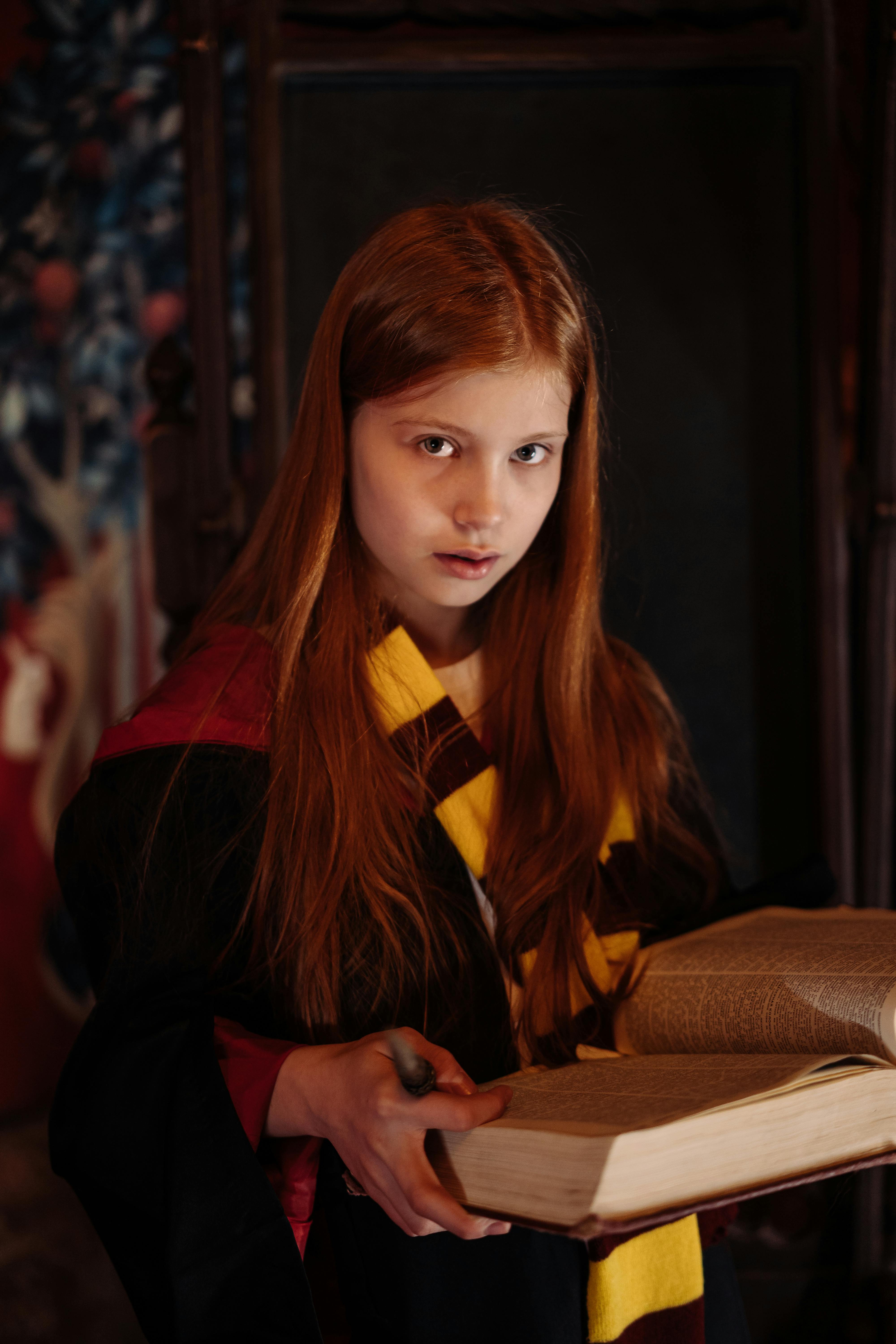 pexels-photo-8389806-8389806 Young girl dressed as a wizard holding an open book indoors, evoking a magical ambiance.